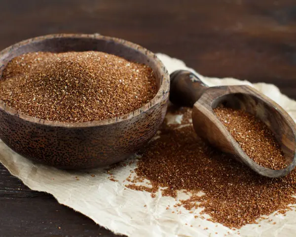 Un cuenco de madera lleno de teff cereal y una pala de madera con más granos.