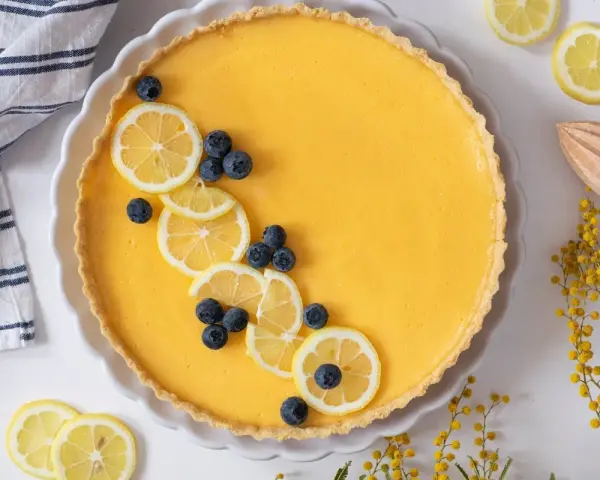 Tarta de limón al horno, decorada con rodajas de limón y arándanos. Un postre refrescante y vibrante.