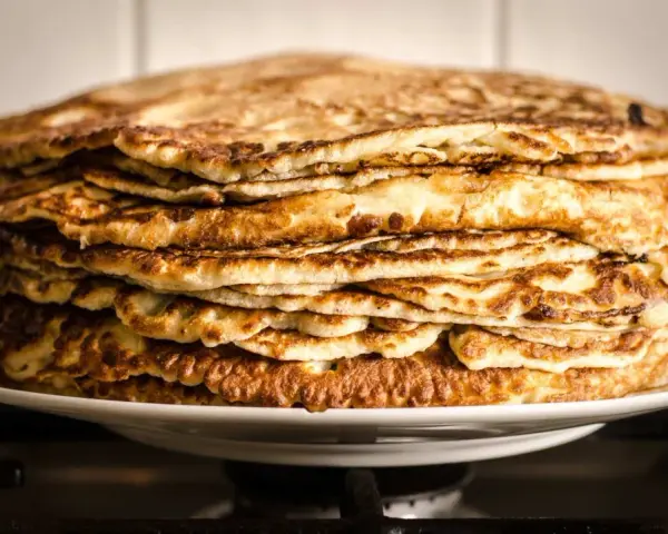Montón de deliciosos pancakes sin gluten, dorados y esponjosos, apilados en un plato blanco.