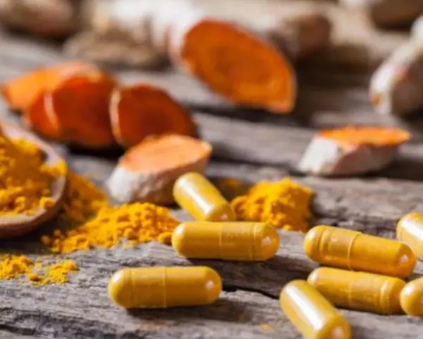 Cápsulas amarillas y polvo de cúrcuma sobre madera rústica, destacando los beneficios de la curcuma en capsulas.