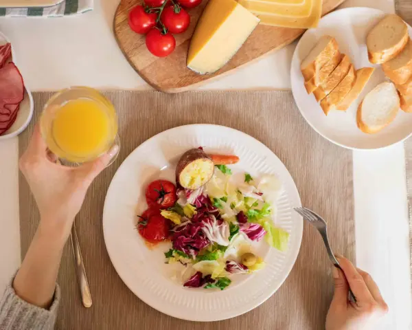 Persona disfrutando una ensalada, tomates, patata asada y un vaso de zumo, parte de su dieta intermitente 16/8.