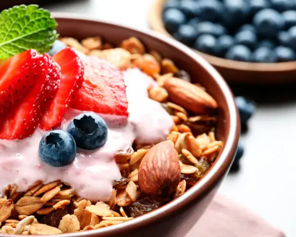 Un tazón de qué es la granola, cubierto con yogur de fresa, fresas, arándanos y almendras.
