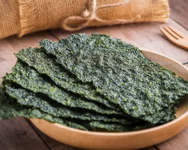 Plato de madera con finas láminas de varios tipos de algas comestibles, listas para disfrutar.