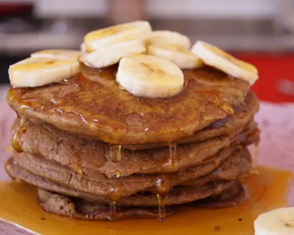 Pila de tortitas de avena y plátano, cubiertas con rodajas de plátano y sirope dorado. ¡Un desayuno delicioso!