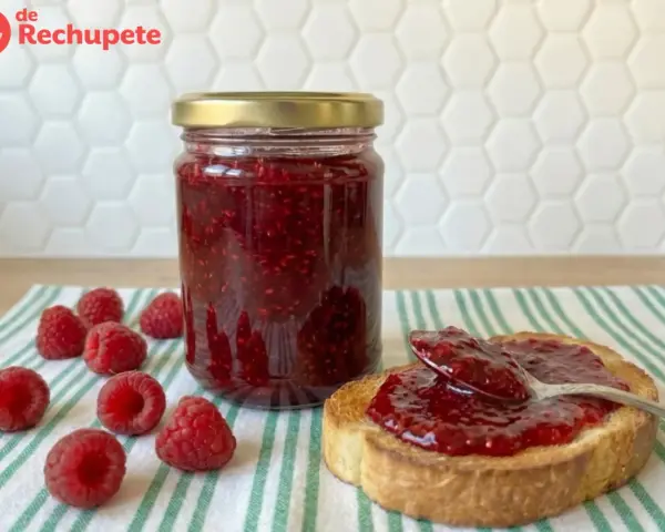 Tarro de mermelada de frambuesa casera, con frambuesas frescas y una tostada untada.