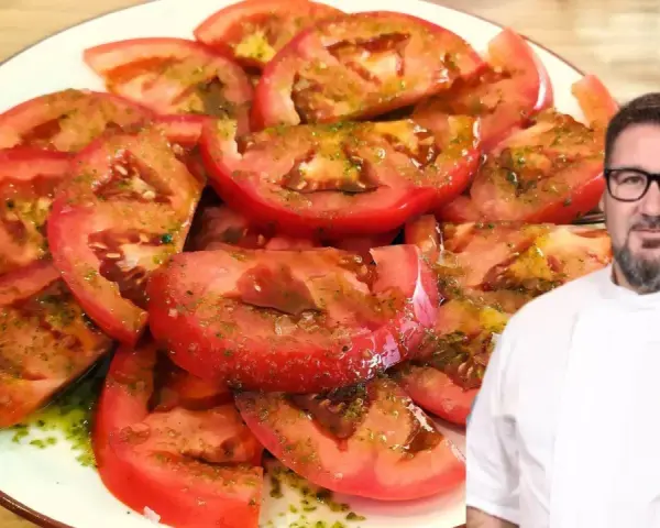 Un chef sonriente presenta un plato de tomate aliñado, fresco y jugoso, con un aderezo verde y aceite.