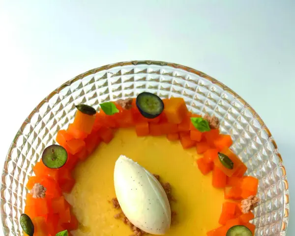 Delicioso flan de mango con helado de vainilla, trozos de mango fresco, arándanos y hojas de menta en un plato de cristal.
