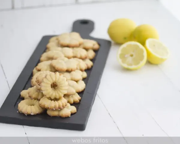 Deliciosas galletas de limón dispuestas en una tabla negra, con limones frescos al lado.