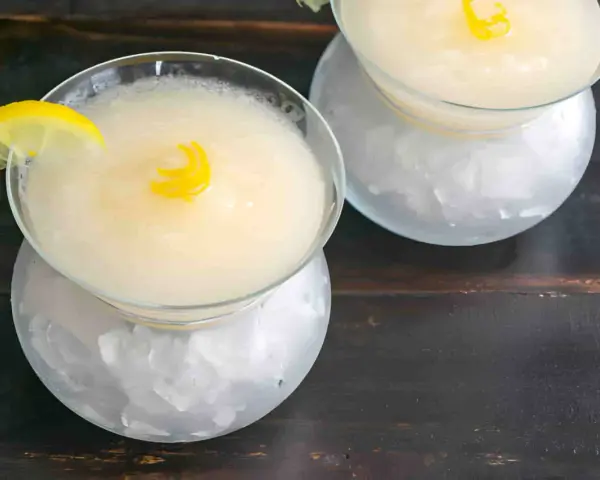 Dos copas de sorbete de limón, una con rodaja de limón y rizo de piel, servidas sobre hielo picado.
