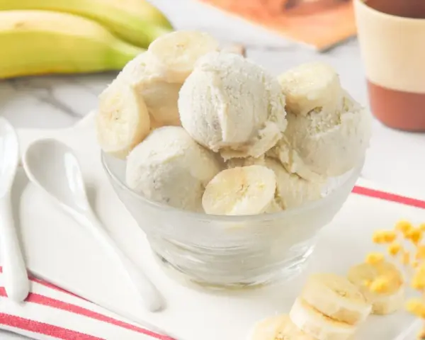 Delicioso helado de platano casero, cremoso y refrescante, servido en un cuenco de cristal con rodajas de plátano fresco.