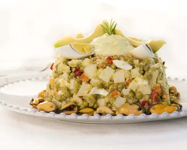 Deliciosa ensaladilla de aguacate con huevo duro, guisantes y mejillones, coronada con una crema suave y rodajas de aguacate fresco.