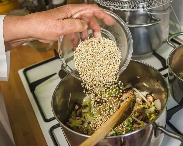 Mano añade trigo sarraceno a una olla con verduras y champiñones.
