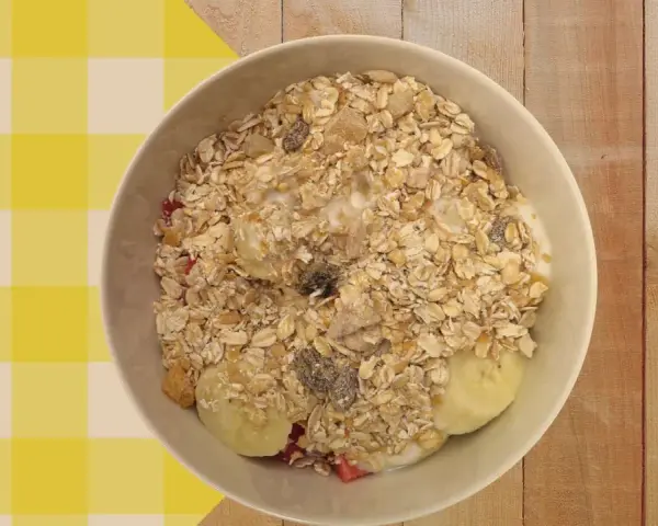 Un tazón de porridge de avena con plátano, fresas y pasas, servido sobre un mantel a cuadros amarillos y blancos.