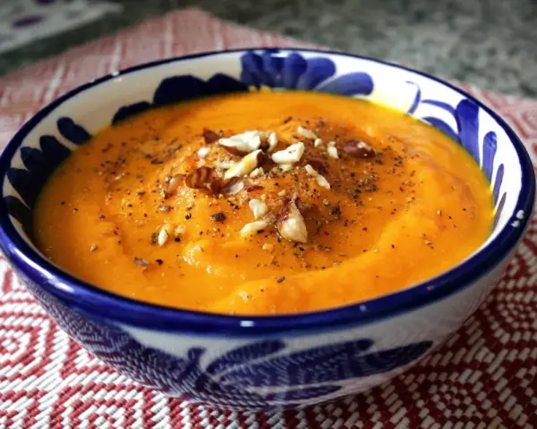 Crema de zanahoria y jengibre, servida en un cuenco azul y blanco, adornada con nueces y pimienta.