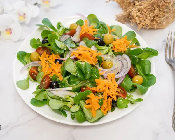 Deliciosa ensalada mediterránea con lechuga, tomate, aceitunas, cebolla morada y zanahoria rallada.