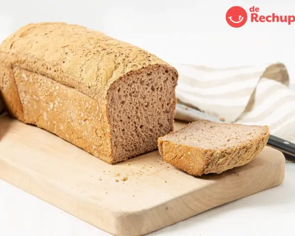 Pan sin gluten recién horneado, con una rebanada lista para disfrutar. Su textura porosa y corteza dorada invitan a probarlo.