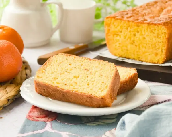 Un delicioso bizcocho de mandarina, recién horneado, con dos rebanadas servidas en un plato blanco.