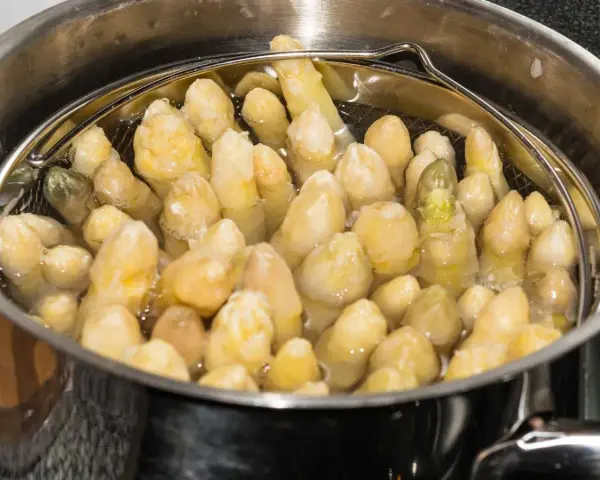 Espárragos blancos tiernos burbujeando en agua, listos para cocer.