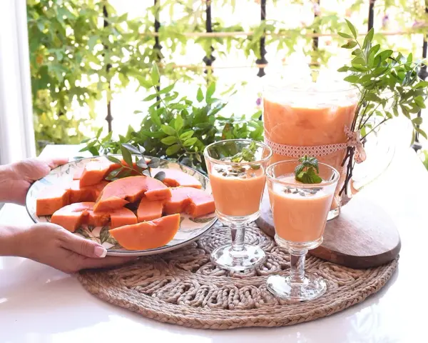 Delicioso zumo de papaya servido en copas y jarra, acompañado de papaya fresca en rodajas.