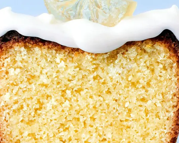 Rebanada de bizcocho esponjoso con un delicioso frosting de limón y una rodaja de limón cristalizado encima.