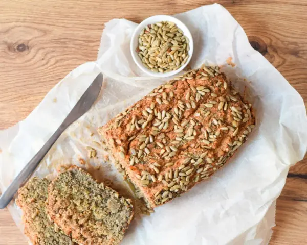 Pan de lentejas casero, cubierto de semillas de girasol, con dos rebanadas y un cuchillo sobre papel de hornear.