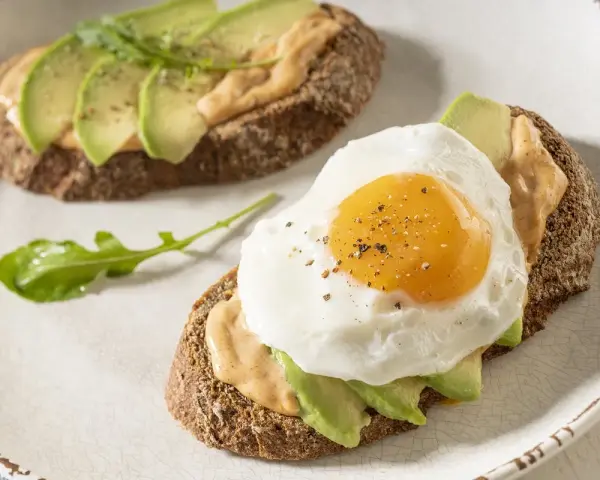Tostas de aguacate para cenar, una con huevo frito y la otra con rúcula. Delicioso y saludable.