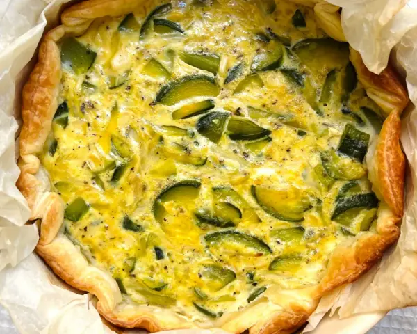 Quiche de calabacín recién horneada, con masa dorada y relleno cremoso salpicado de trozos verdes.