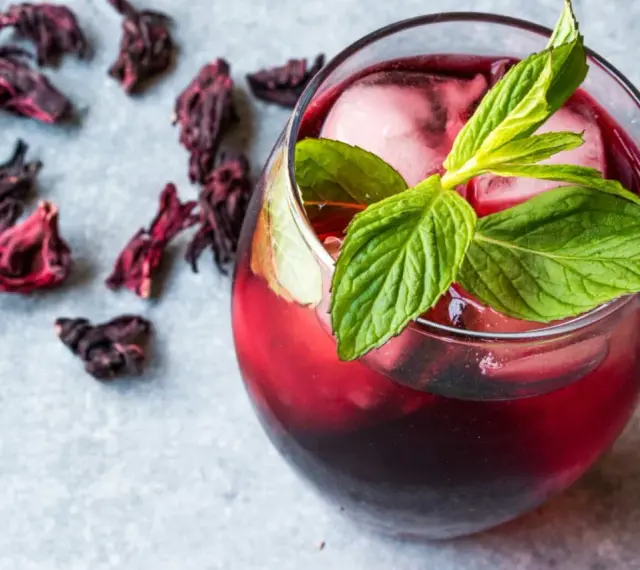 Refrescante vaso de agua de jamaica con hielo y menta, rodeado de flores secas de hibisco.