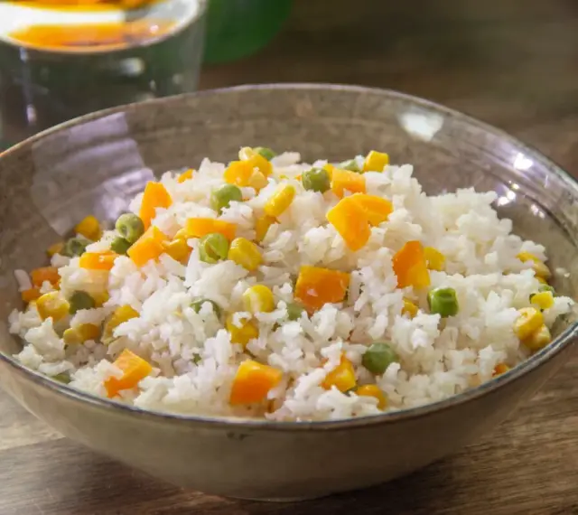 Un tazón de arroz blanco con trozos de zanahoria, guisantes y maíz. Un plato sencillo y colorido de arroz con verduras.