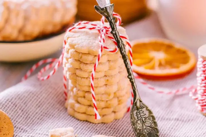 Deliciosas galletas de naranja, apiladas y atadas con hilo rojo y blanco. Una rodaja de naranja y una cuchara antigua completan la escena.
