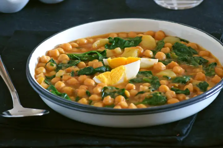 Plato humeante de garbanzos con espinacas y huevo duro, una deliciosa receta de garbanzos tradicional.