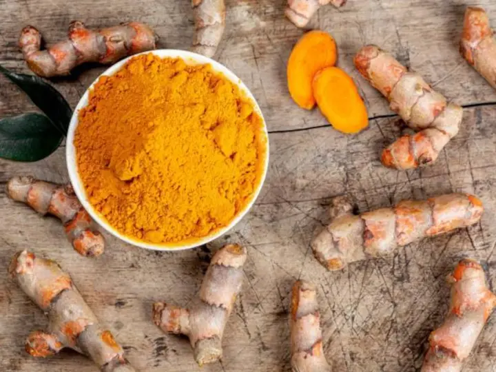 Raíces de cúrcuma y polvo dorado en un cuenco. Descubre qué es la cúrcuma y para qué sirve, un tesoro natural.