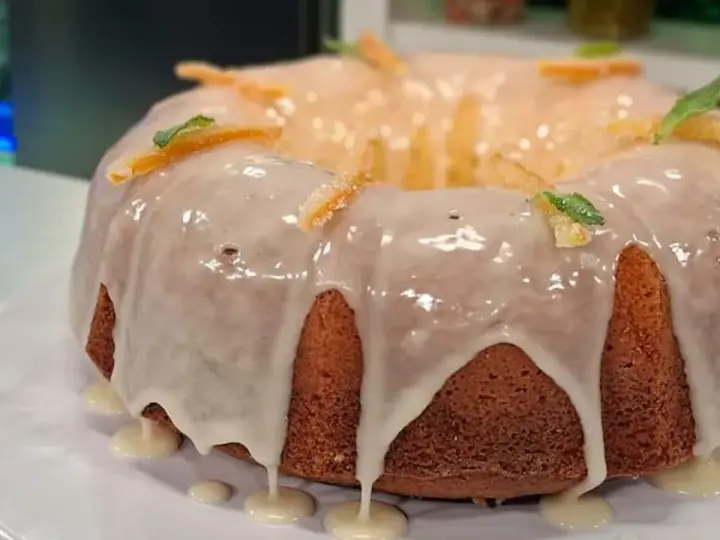 Delicioso budín de naranja con glaseado blanco y decorado con cáscaras de naranja confitada y hojas de menta.