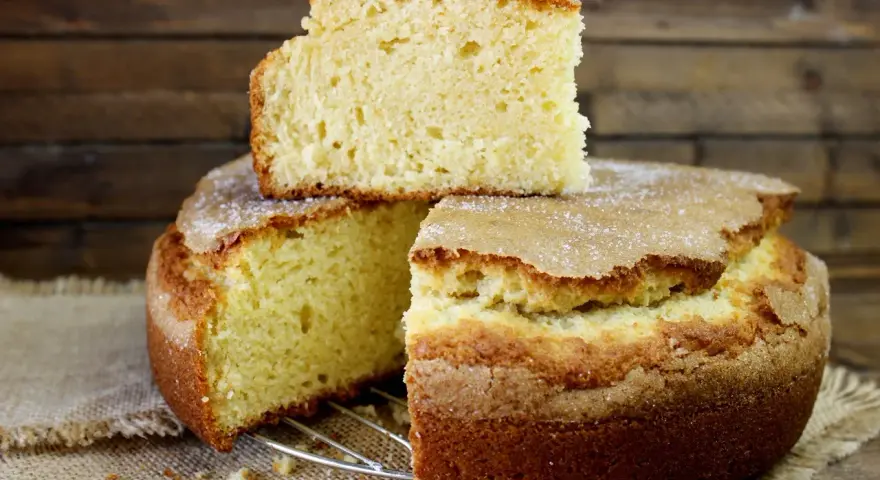 El bizcocho de limón de la abuela, esponjoso y dorado, con una capa de azúcar espolvoreada. Un trozo descansa sobre el pastel principal.