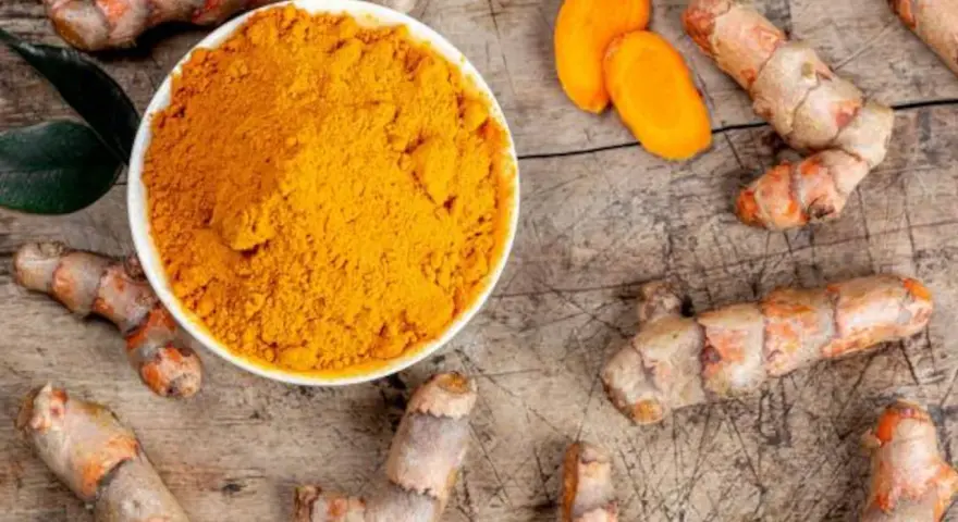 Raíces de cúrcuma y polvo dorado en un cuenco. Descubre qué es la cúrcuma y para qué sirve, un tesoro natural.