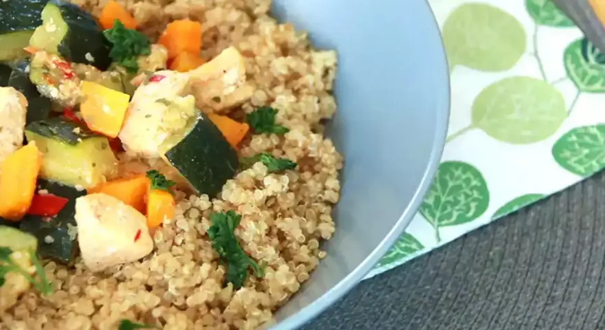 Un tazón de quinoa con pollo y verduras salteadas, como calabacín y zanahoria.