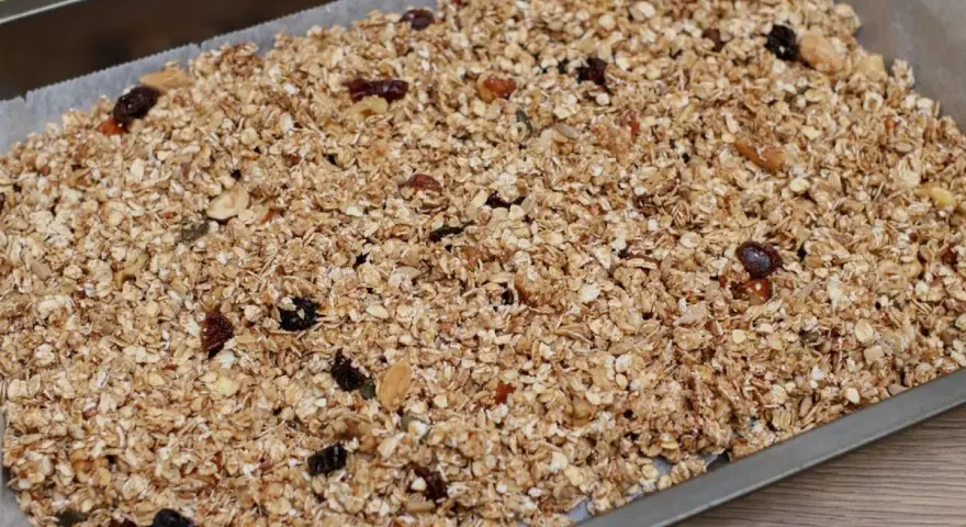 Granola de avena casera lista para hornear, con frutos secos y pasas, extendida en una bandeja.