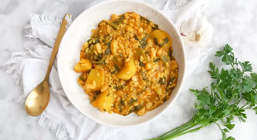 Un tazón de arroz con acelgas, patatas y alubias blancas, servido con una cuchara dorada y perejil fresco.