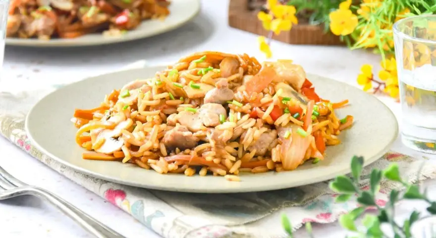 Un delicioso wok de verduras y arroz con trozos de pollo y champiñones, adornado con cebollino fresco.