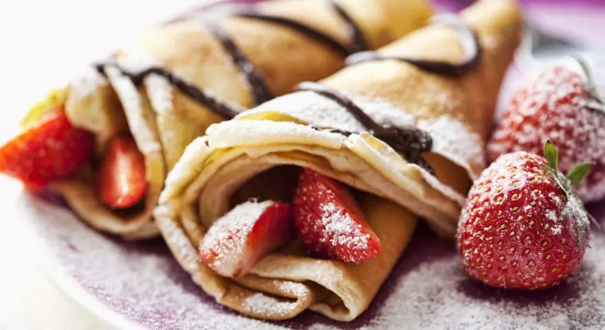Deliciosos crepes sin huevo rellenos de fresas y bañados en chocolate, espolvoreados con azúcar glas.