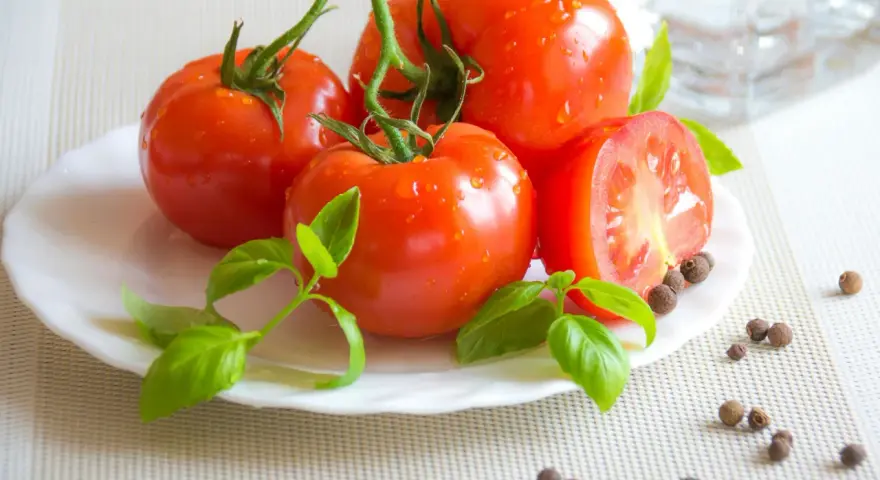 Tomates frescos con gotas de agua, albahaca y granos de pimienta, ingredientes naturales para productos antiinflamatorios.