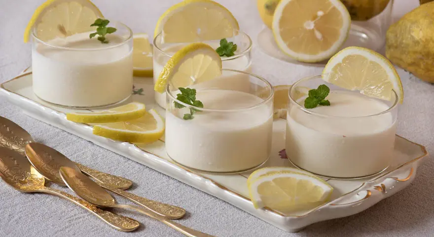 Delicioso postre de lemon curd receta original, servido en vasos con rodajas de limón y menta.