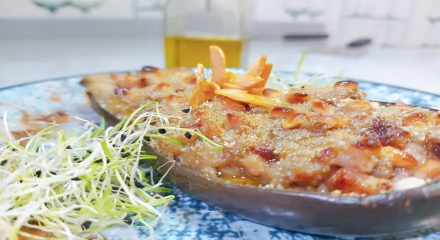 Deliciosa berenjena rellena gratinada, adornada con piñones y brotes frescos, lista para ser disfrutada.