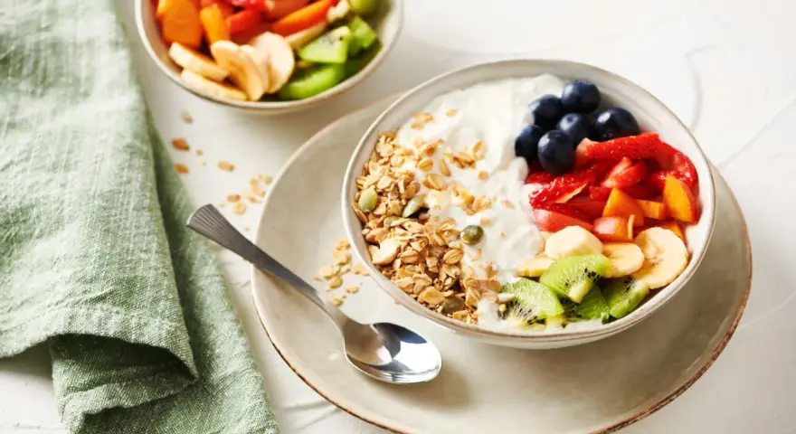 Un tazón de yogur cremoso con granola crujiente, arándanos, fresas, plátano, kiwi y melocotón.