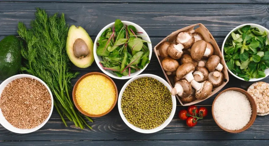 Variedad de alimentos ricos en proteinas vegetales: aguacate, hinojo, lentejas, champiñones, arroz, tomates y hojas verdes.