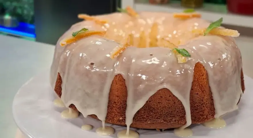Delicioso budín de naranja con glaseado blanco y decorado con cáscaras de naranja confitada y hojas de menta.