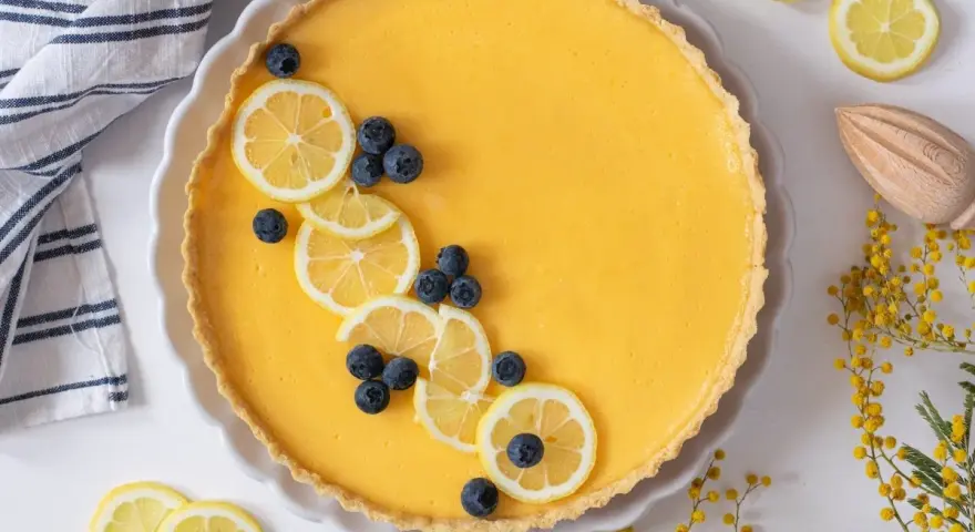 Tarta de limón al horno, decorada con rodajas de limón y arándanos. Un postre refrescante y vibrante.