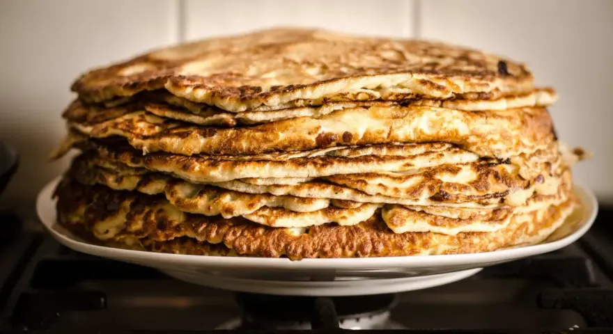Montón de deliciosos pancakes sin gluten, dorados y esponjosos, apilados en un plato blanco.