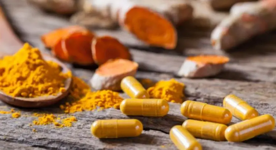 Cápsulas amarillas y polvo de cúrcuma sobre madera rústica, destacando los beneficios de la curcuma en capsulas.