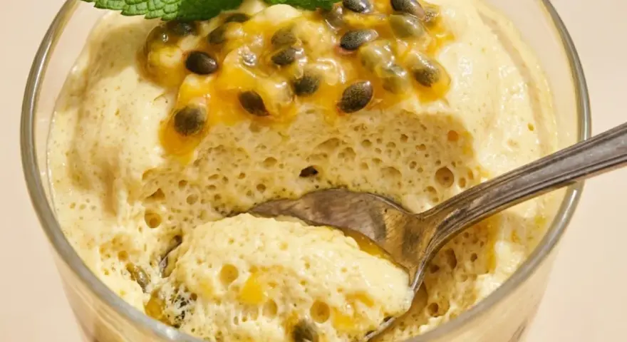 Delicioso mousse de maracuyá en vaso, coronado con pulpa y semillas de la fruta, y una hoja de menta. Una cucharada lista para disfrutar.